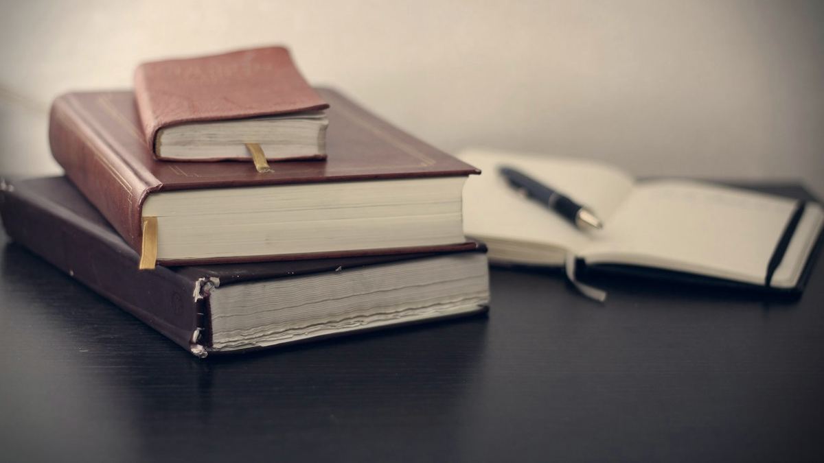 Livros encadernados e um caderno aberto com caneta sobre a mesa